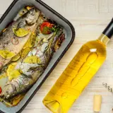 Zwei gebackene Forellen mit Zitrone und Kräutern, daneben eine Flasche Weißwein und ein Glas. Perfekt, welcher Wein zu Lachs passt, ist hier schon fast klar.