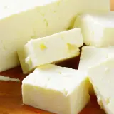 Frischer Feta, leicht schleimig, liegt auf einem Holzbrett, daneben grüne Basilikumblätter.