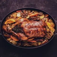 Ein goldbraun gebratener Gänsebraten mit Kartoffeln, Karotten und Orangenscheiben. Perfekt für die Frage: welcher Wein zu Gans?