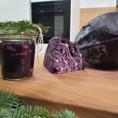 Ein Glas mit fermentiertem Rotkohl, daneben ein halber und ein ganzer Rotkohl. Tannenzweige schmücken das Glas.