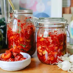 Zwei Gläser mit fermentierter Melone, daneben eine Wassermelone, Frühlingszwiebeln und eine Flasche.