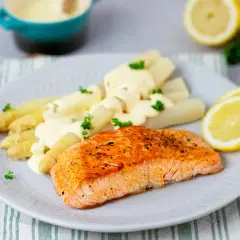 Gebratener Lachs mit weißem Spargel und cremiger Hollandaise. Ein klassisches Rezept mit Holllandaise, garniert mit Petersilie und Zitronenscheiben.
