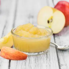Apfelmus in einer Schale, umgeben von Apfelstücken und ganzen Äpfeln. Perfekt für leckere Rezepte mit Apfelsaft.