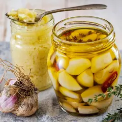 Eingelegter Knoblauch in Öl, daneben ein Glas mit Knoblauchpaste. So legt man Knoblauch ein für mehr Aroma.