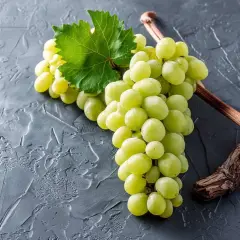 Grüne Trauben, die an einem Rebstock hängen. Diese Trauben sind ein Beispiel dafür, was Chardonnay ist: eine beliebte Rebsorte für Weißwein.