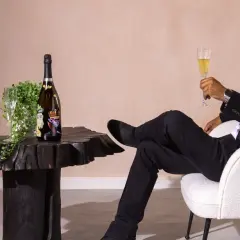 Ein Mann in schwarzem Anzug genießt ein Glas Champagner neben einer Flasche, die wie der teuerste Champagner der Welt aussieht.