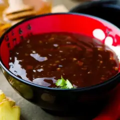 Schwarze Schüssel mit glänzender, dunkler Teriyaki-Sauce, umgeben von frischem Ingwer und Chili.