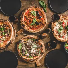 Vier verschiedene Pizzen, ein Salat und Rotwein auf Holztisch. Die Frage welcher Wein zu Pizza wird hier stilvoll beantwortet.