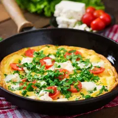Herzhaftes Omelette mit Feta, Tomaten und Petersilie in einer Pfanne, bereit zum Servieren.
