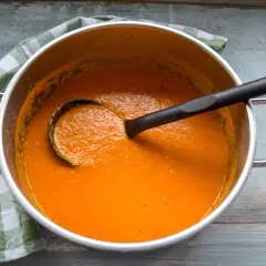 Ein Topf mit cremiger roter Linsensuppe mit Kokosmilch, bereit zum Servieren. Ein grünes Karotuch liegt daneben.