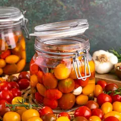 Gläser mit bunten Kirschtomaten, bereit zum **Tomaten fermentieren**. Daneben Knoblauch, Rosmarin und Pfefferkörner.