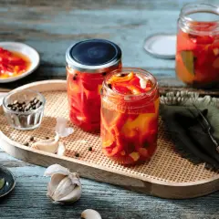 Zwei Gläser mit eingelegten Paprikastreifen, Knoblauch, Pfefferkörnern und Lorbeerblättern. Der Prozess des Paprika fermentieren ist hier gut sichtbar.