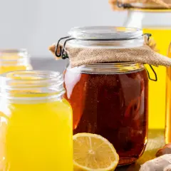 Gläser mit gelbem Getränk und ein großes Glas mit dunklem, sprudelndem fermentiertem Honig, daneben Zitronen und Ingwer.