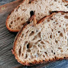 Zwei Scheiben rustikales, fermentiertes Brot liegen auf einer Holzoberfläche. Die Krume ist luftig und voller großer Poren.