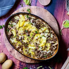 Herzhafter kartoffelauflauf aus rohen Kartoffeln mit Hackfleisch, überbacken mit Käse. Garniert mit Petersilie und Lauch.