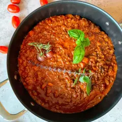 Herzhafte rotwein bolognese in einer Pfanne, garniert mit Basilikum und Kirschtomaten.