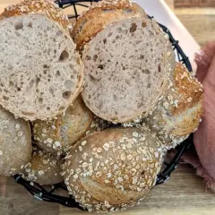 Korb mit knusprigen Haferbrot-Brötchen, eines davon aufgeschnitten, zeigt die luftige Krume.