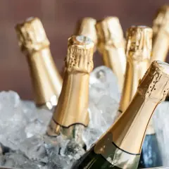 Mehrere Champagnerflaschen in goldenen Kapseln kühlen in einem Eisbad. Die perfekte Champagner Temperatur für den Genuss.