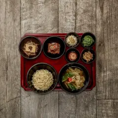 Korean temple food: eine Schale Reis, Tofu, Kimchi und verschiedene Gemüsebeilagen auf einem roten Tablett.