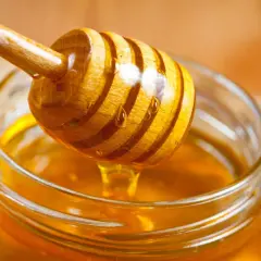 Ein Honigheber aus Holz tropft goldenen Honig in ein Glas. Kein Anzeichen von honig schimmel.
