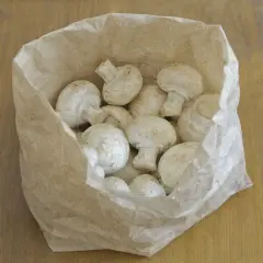 Frische Champignons lagern in einer Papiertüte auf einem Holztisch.