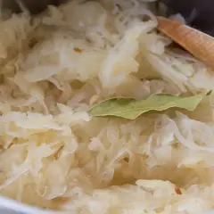 Frisch zubereitetes Sauerkraut mit Lorbeerblatt und einem Holzlöffel. Perfekt als Beilage zu einem herzhaften Gericht, vielleicht mit einem Glas Wein.