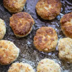 Mehrere goldbraune hackfleisch frikadellen brutzeln in heißem Öl in einer Pfanne.