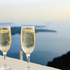 Zwei Gläser Champagner mit Bläschen stehen vor einer Meereslandschaft. Die Frage, wie lange ist Champagner haltbar, beschäftigt Genießer.