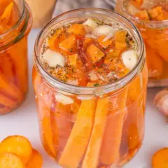 Gläser mit karotten fermentieren, gefüllt mit Karottenstücken, Knoblauch und Kräutern. Ein ganzer Knoblauch liegt daneben.