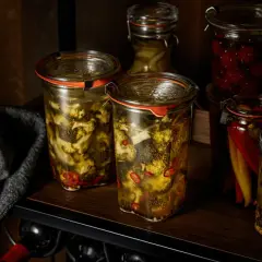 Zwei Gläser mit **brokkoli fermentieren**, daneben eingelegte Chilis und Kirschen.