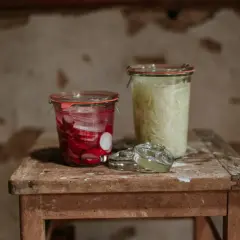 Zwei Gläser mit fermentierten Lebensmitteln: links eingelegte Radieschen, rechts fermentiertes Sauerkraut.