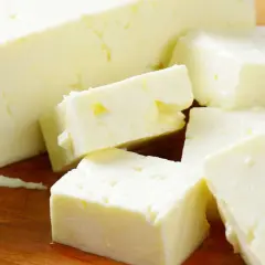 Frischer Feta, leicht schleimig, liegt auf einem Holzbrett, daneben grüne Basilikumblätter.