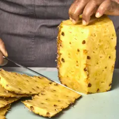 Hände schneiden eine Ananas. Dunkle Flecken auf der Frucht könnten ein Hinweis sein, um Ananas Schimmel zu erkennen.