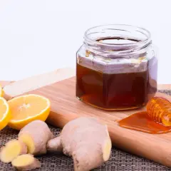 Zutaten für ingwer-honig zitrone ansetzen: frischer Ingwer, Zitronenscheiben und ein Glas Honig mit Honigheber.