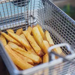 Goldgelbe Pommes in einem Frittierkorb, bereit, um sie wieder knusprig zu machen.