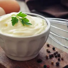 Frische Eier und Petersilie auf einem Holzbrett, bereit, um köstliche Mayonnaise selber zu machen. Ein Schneebesen liegt daneben.