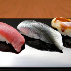 Drei exquisite Sushi-Rollen auf schwarzer Platte: roter Thunfisch, silberner Fisch mit Schuppen und ein mit Soße überzogener Fisch. Das teuerste Sushi der Welt, ein kulinarischer Genuss.