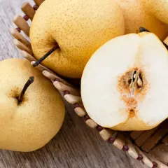 Nashi Birnen, deren Herkunft in Asien liegt, in einem Korb. Eine Frucht ist halbiert und zeigt das saftige Innere.