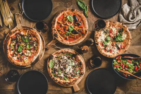 Vier verschiedene Pizzen, ein Salat und Rotwein auf Holztisch. Die Frage welcher Wein zu Pizza wird hier stilvoll beantwortet.