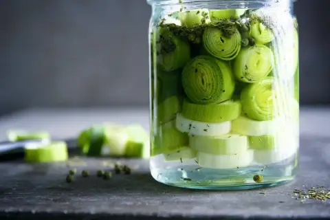 Ein Glas mit geschnittenem Lauch, bereit zum lauch fermentieren. Grüne Pfefferkörner und Kräuter sind ebenfalls zu sehen.