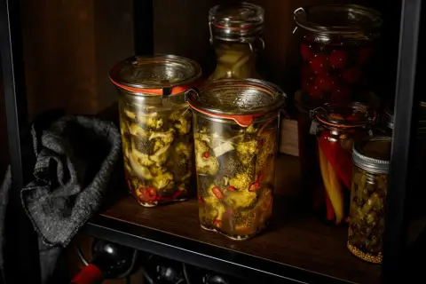 Zwei Gläser mit **brokkoli fermentieren**, daneben eingelegte Chilis und Kirschen.