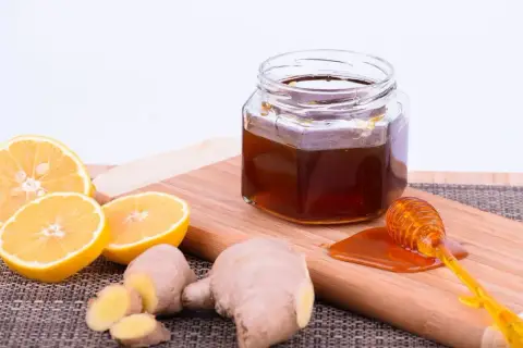 Zutaten für ingwer-honig zitrone ansetzen: frischer Ingwer, Zitronenscheiben und ein Glas Honig mit Honigheber.