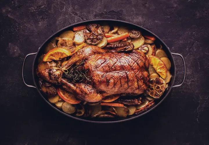 Ein goldbraun gebratener Gänsebraten mit Kartoffeln, Karotten und Orangenscheiben. Perfekt für die Frage: welcher Wein zu Gans?