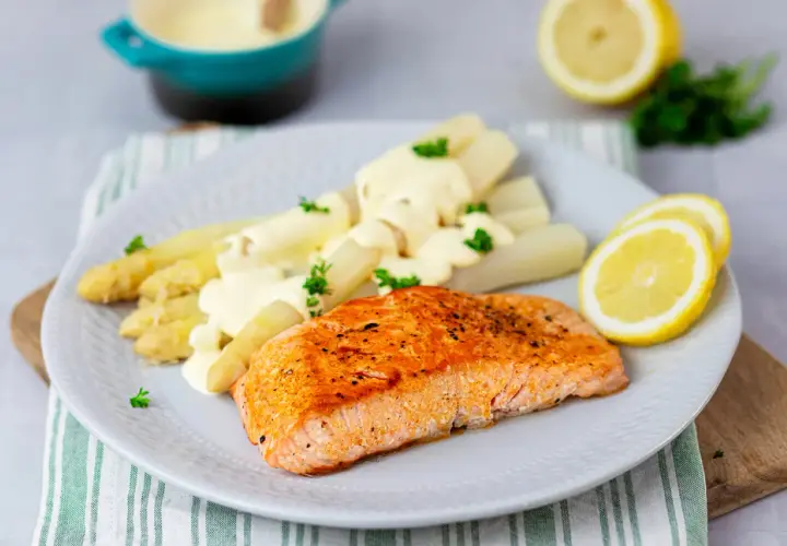 Gebratener Lachs mit weißem Spargel und cremiger Hollandaise. Ein klassisches Rezept mit Holllandaise, garniert mit Petersilie und Zitronenscheiben.