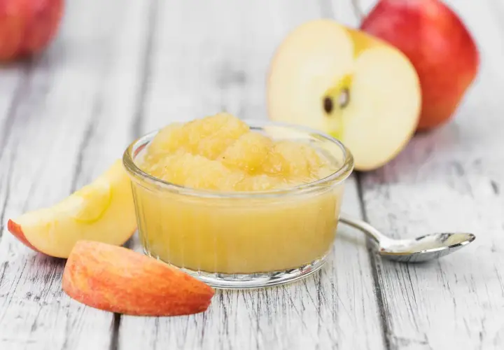 Apfelmus in einer Schale, umgeben von Apfelstücken und ganzen Äpfeln. Perfekt für leckere Rezepte mit Apfelsaft.
