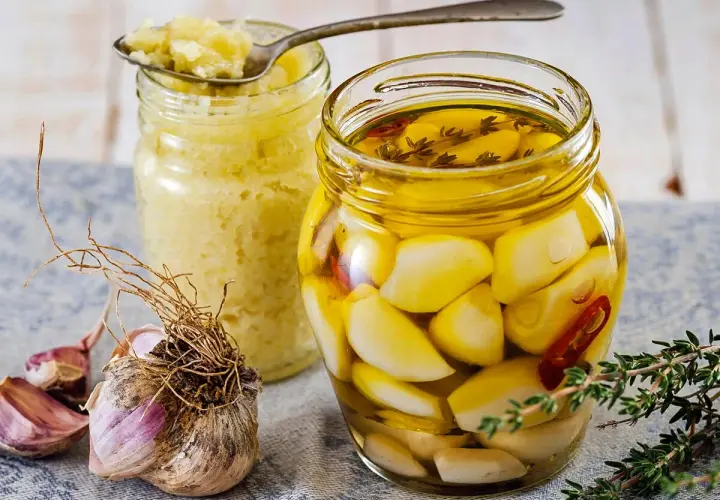 Eingelegter Knoblauch in Öl, daneben ein Glas mit Knoblauchpaste. So legt man Knoblauch ein für mehr Aroma.