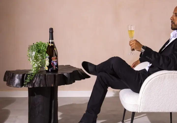 Ein Mann in schwarzem Anzug genießt ein Glas Champagner neben einer Flasche, die wie der teuerste Champagner der Welt aussieht.