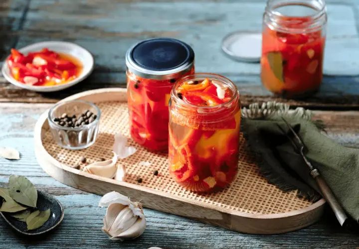 Zwei Gläser mit eingelegten Paprikastreifen, Knoblauch, Pfefferkörnern und Lorbeerblättern. Der Prozess des Paprika fermentieren ist hier gut sichtbar.