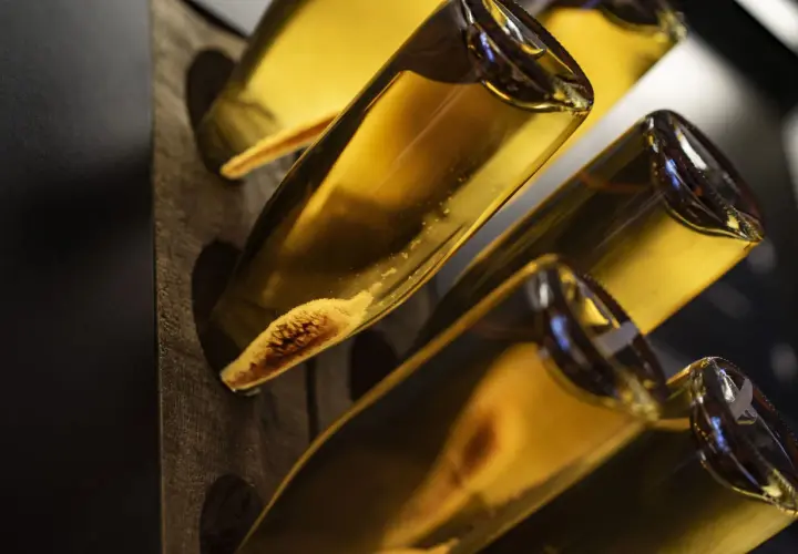 Flaschen mit goldgelbem Inhalt, vielleicht ein cremiger Wein oder ein süßer Likör. Die Sedimente am Flaschenboden deuten auf eine traditionelle Herstellung hin.