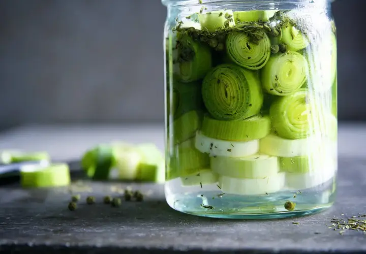 Ein Glas mit geschnittenem Lauch, bereit zum lauch fermentieren. Grüne Pfefferkörner und Kräuter sind ebenfalls zu sehen.